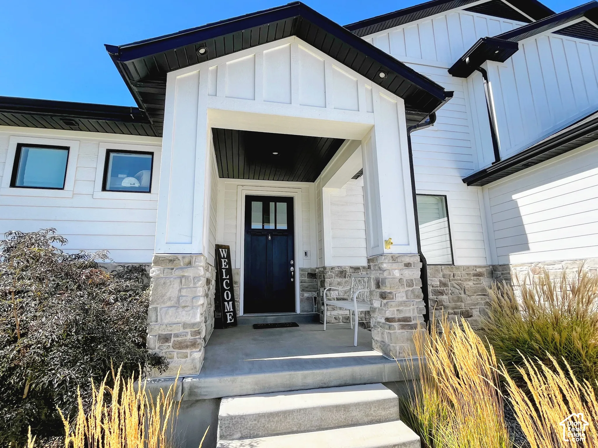 Modern exterior featuring white siding, black trim, a covered porch, stone accents, and a dark entry door with glass panels