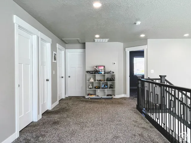 Carpeted hallway with multiple paneled doors, recessed lighting, and a dark metal stair railing