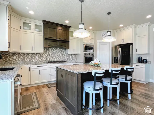 Wood-finish flooring leading to a kitchen with white cabinetry, a dark wood-stained island with a granite countertop, and stainless steel appliances