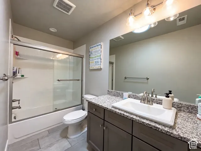 Bathroom featuring a white tub with sliding glass doors, a vanity with a rectangular undermount sink, granite-style countertop, and gray cabinetry