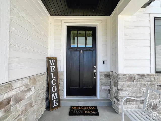 Modern black entry door with upper glass panels, complemented by white horizontal siding, stone-clad foundation, and a contrasting dark soffit