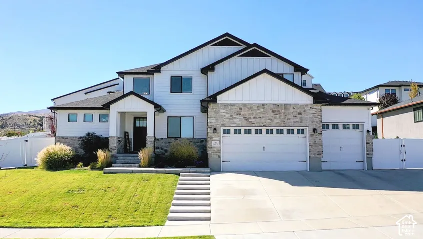 Contemporary exterior with white siding, stone accents, black-framed windows, a covered entry, and multiple garage doors