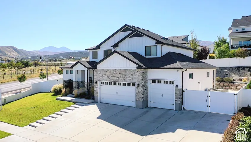 Contemporary architecture featuring a multi-car garage, stone and siding facade, concrete driveway with integrated stepping stones, and a fenced yard with mature landscaping
