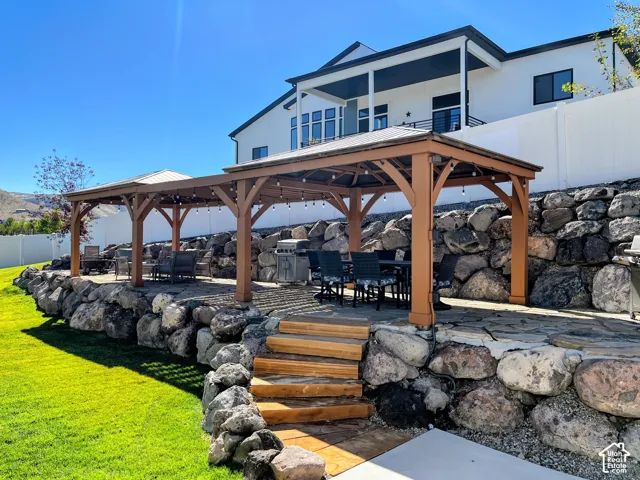 Expansive outdoor living area featuring a stone patio, two large wooden pergolas with string lighting, and a terraced rock retaining wall