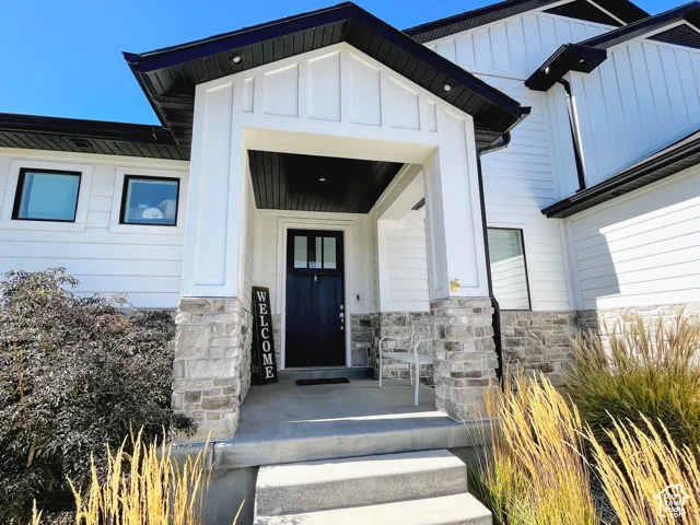 Modern exterior featuring white siding, black trim, a covered porch, stone accents, and a dark entry door with glass panels