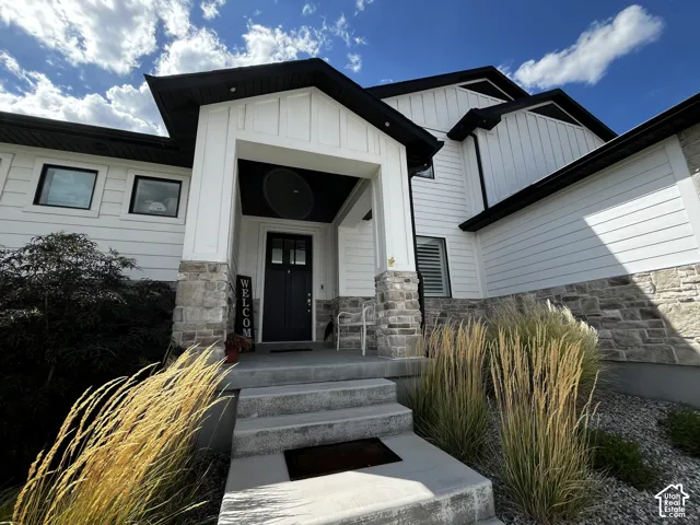 White exterior siding with dark trim accents, natural stone foundation, covered porch entry, and a dark paneled front door