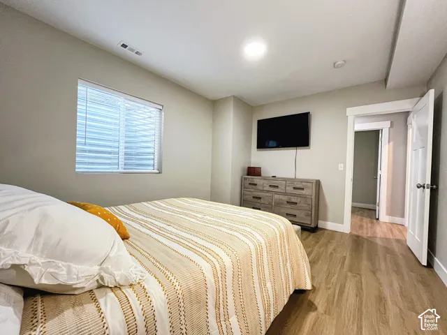 Light wood-finish flooring, recessed lighting, and a white interior door with contemporary hardware