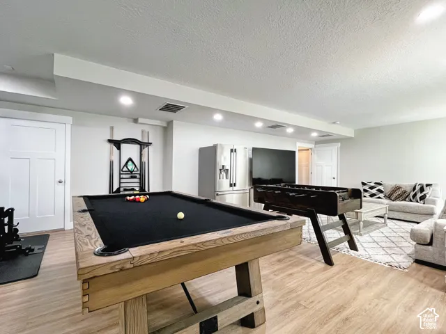 Recessed lighting illuminates the open area featuring wood-finish flooring, white paneled doors, and a built-in dry bar with a stainless steel refrigerator