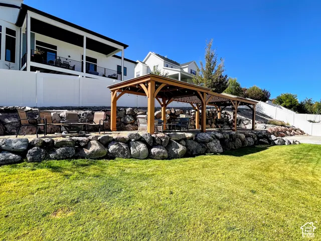Expansive lawn area with a multi-level rock retaining wall, featuring a large wooden pergola with string lighting