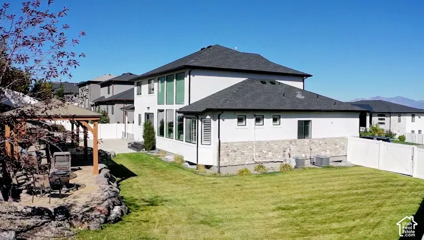 Expansive backyard featuring a manicured lawn, stone retaining walls, a wood-frame gazebo, and a privacy fence