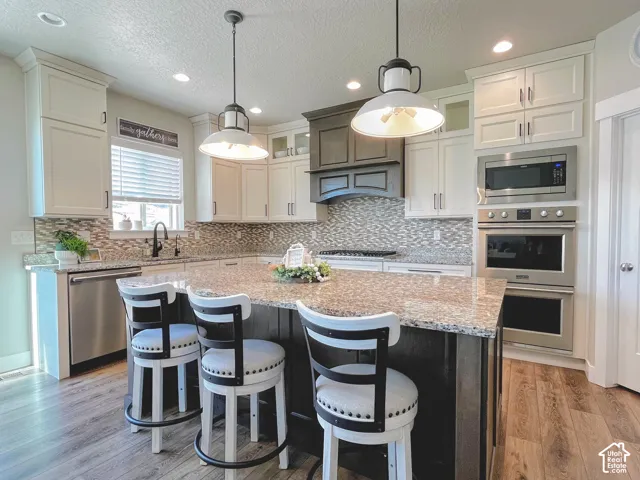 Spacious kitchen featuring a large island with a stone-finish countertop, stainless steel built-in appliances, extensive cabinetry, a tiled backsplash, and recessed lighting