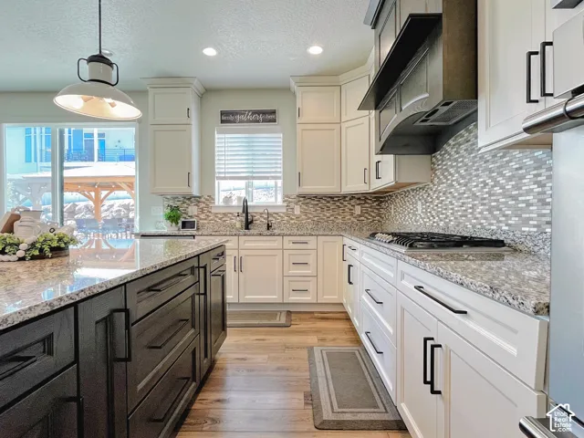 Kitchen featuring white cabinetry, a dark-toned island, light-toned countertops, a patterned tile backsplash, and wood-finish flooring
