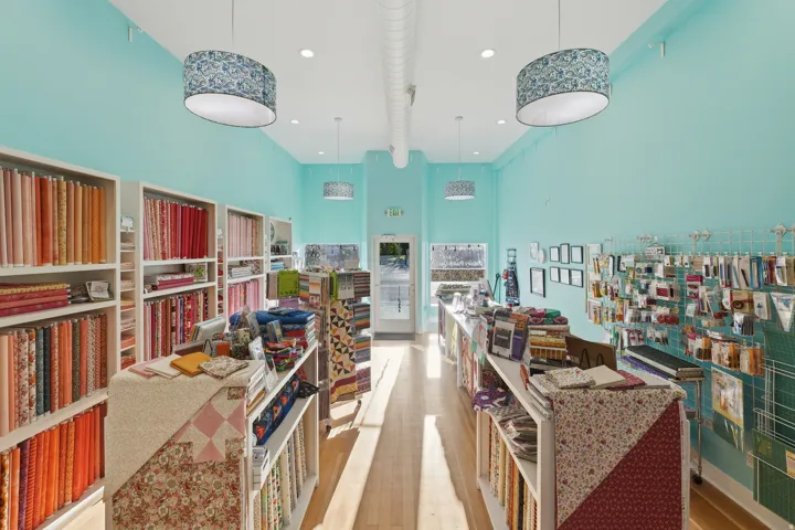 Open retail space featuring light wood-finish flooring, recessed ceiling lighting, and pendant light fixtures
