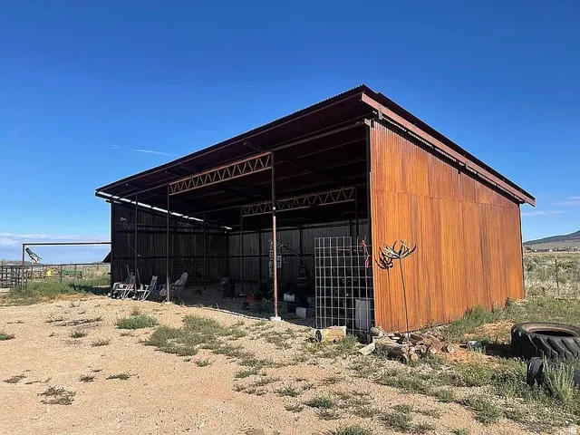 Corrugated metal shed with an open-sided design, featuring a corrugated roof and exposed structural beams