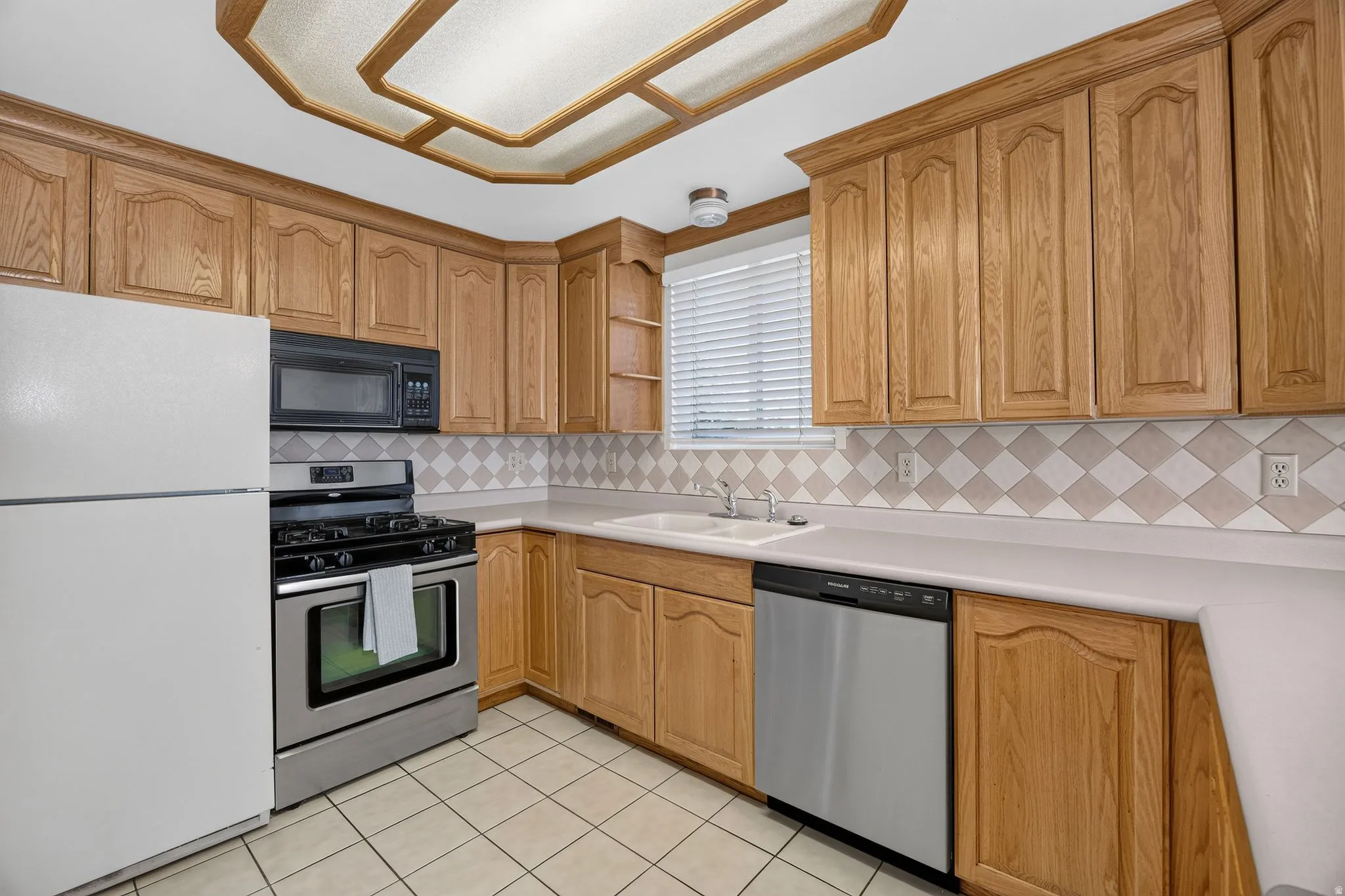 Wood-finish cabinetry, stainless steel range, stainless steel dishwasher, tile flooring, and a decorative ceiling fixture