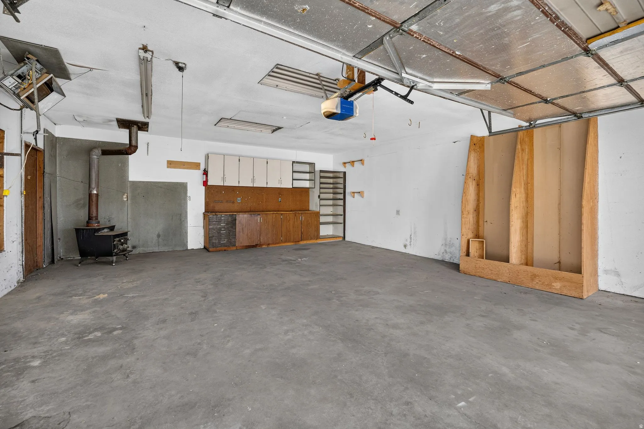 Interior garage, 4-car space, featuring a space heater, a wood-burning stove, built-in cabinetry, and exposed ceiling joists
