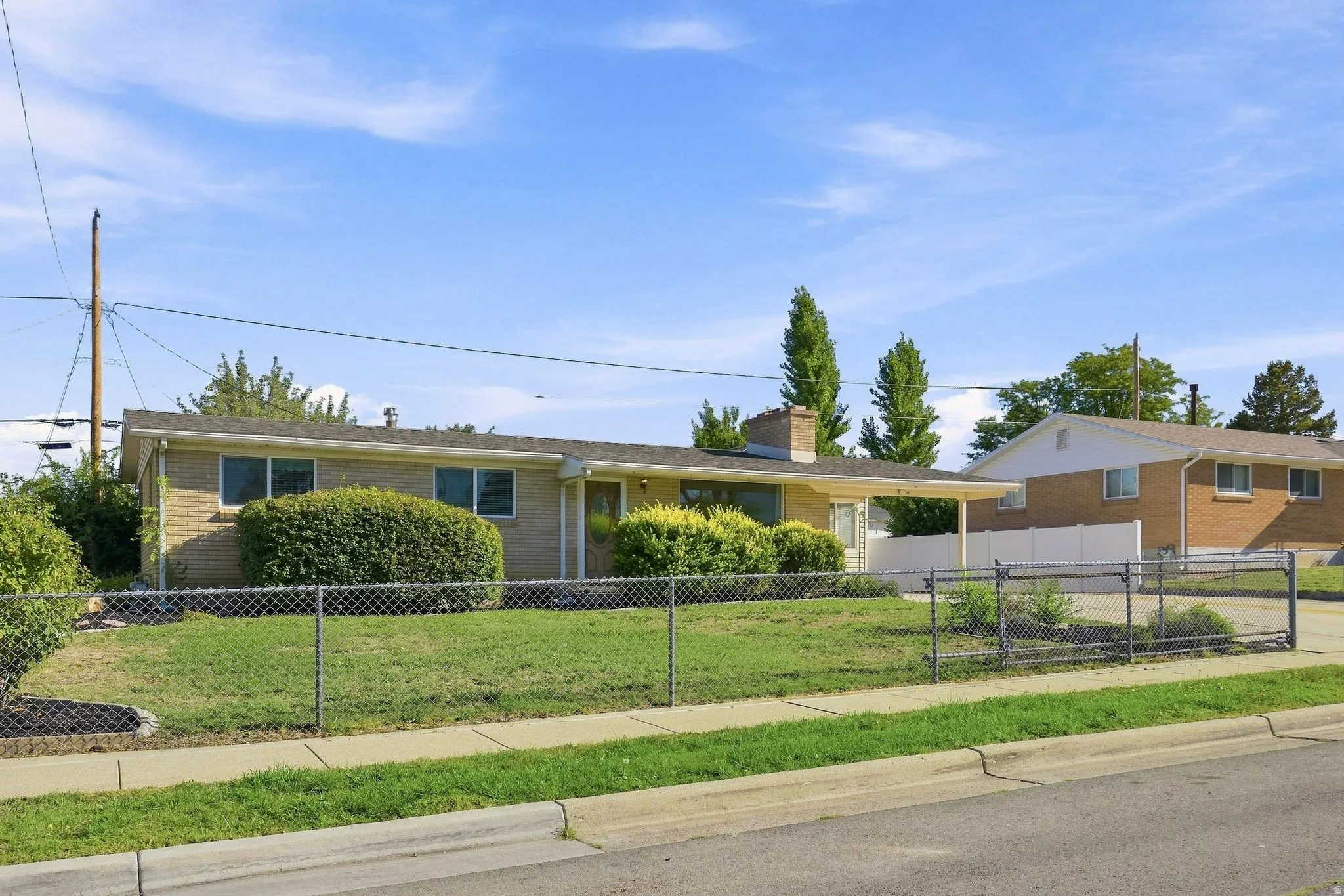 Brick exterior with a covered entryway, covered front patio and porch, chain-link fencing, and mature landscaping