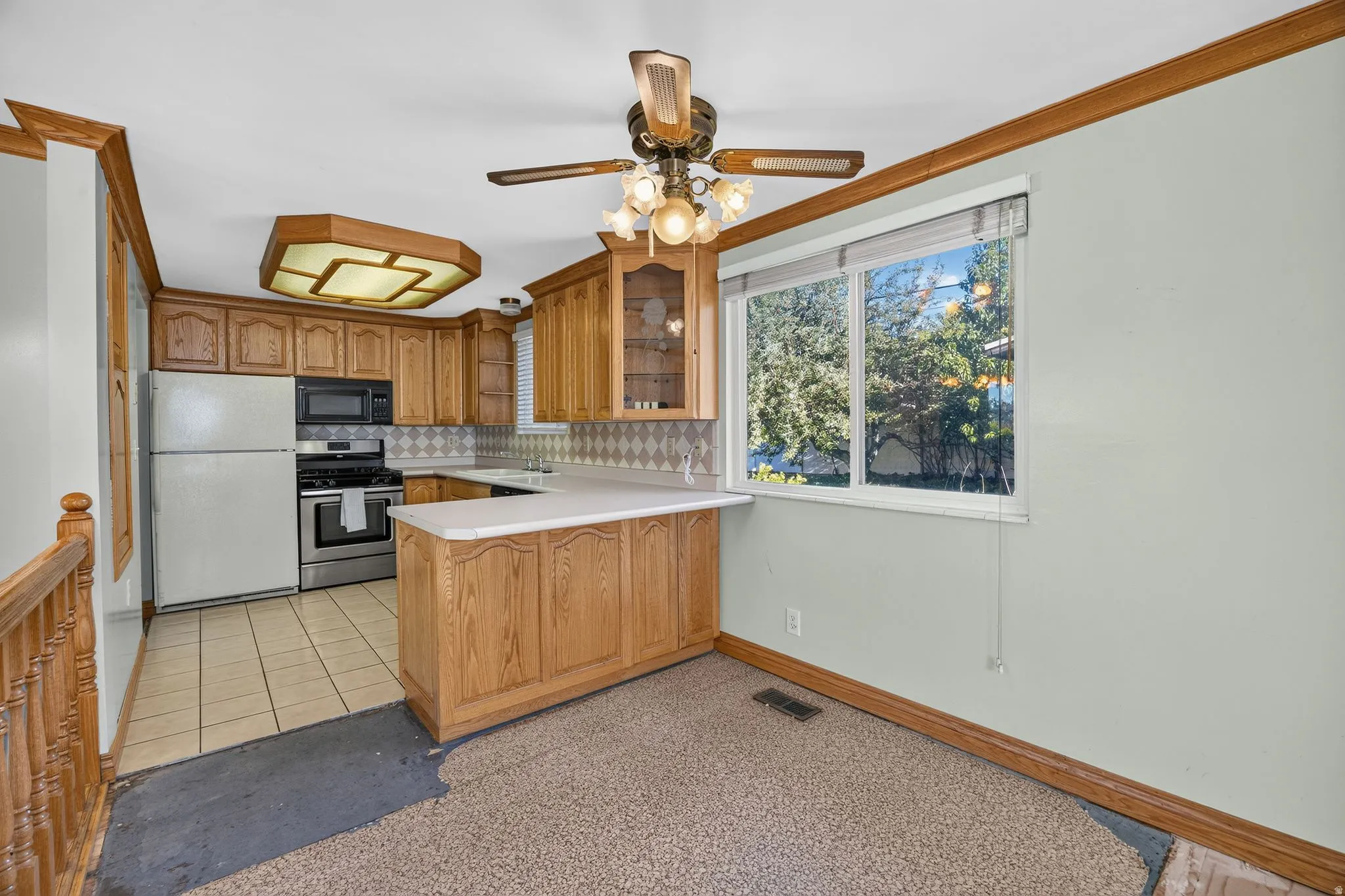 Kitchen featuring wood cabinetry, white countertops, stainless steel appliances, and a ceiling fan with integrated lighting