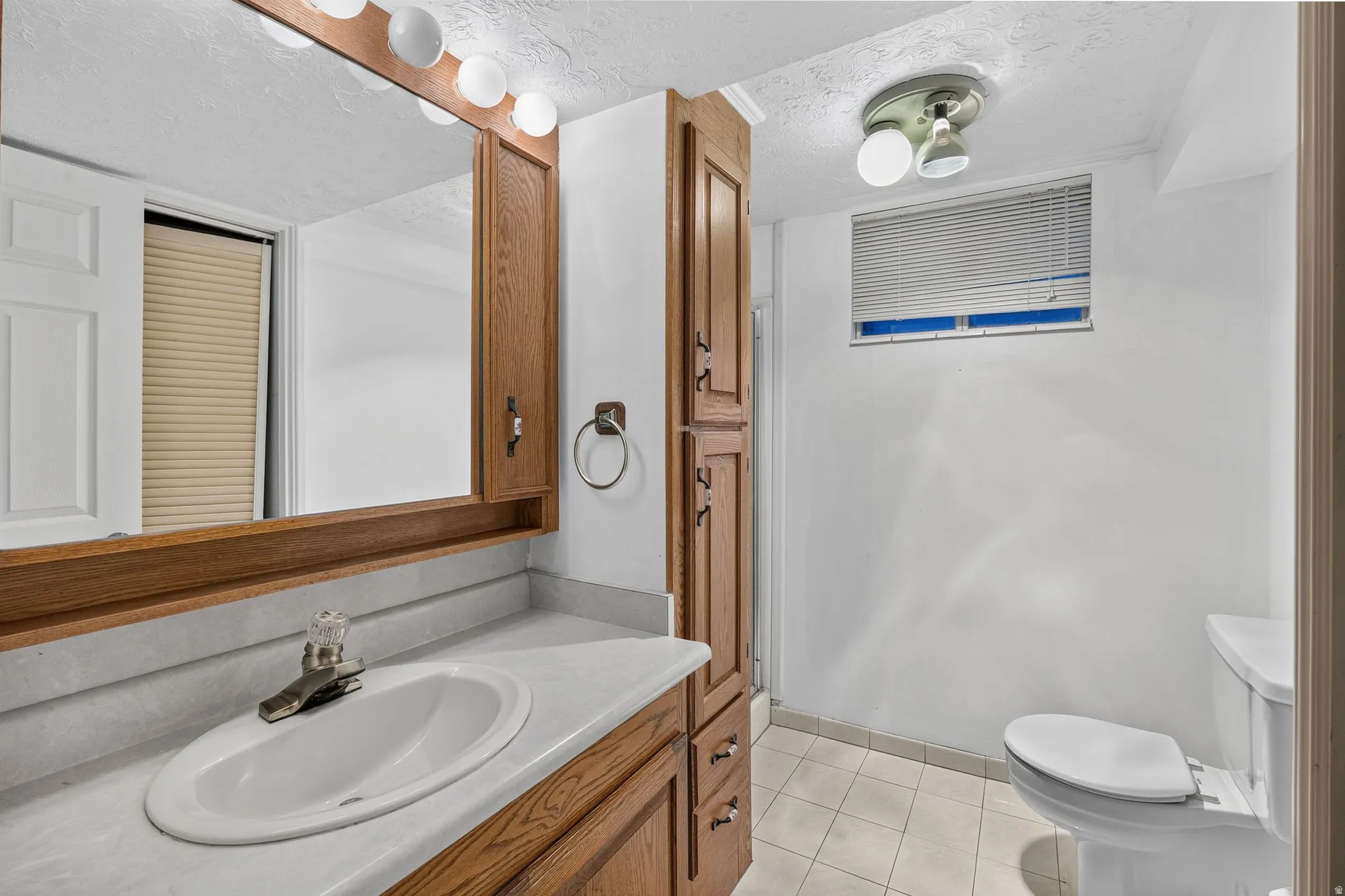 Vanity with integrated sink, wood-finish cabinetry, full-width mirror, and overhead lighting