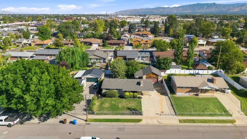 Aerial depiction of a residential street with multiple single-story homes, mature landscaping, and mountain ranges in the distance
