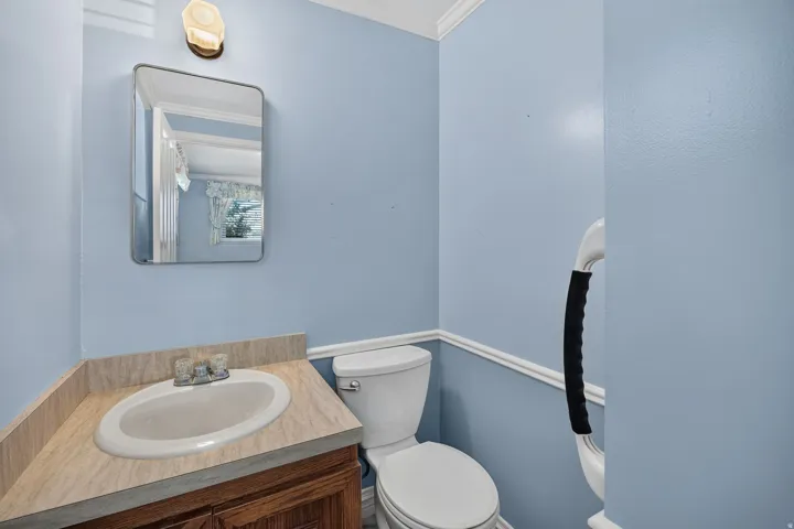 Primary Suite half bath, vanity with an oval basin sink and a laminate countertop, accented by a wall-mounted mirror and overhead lighting