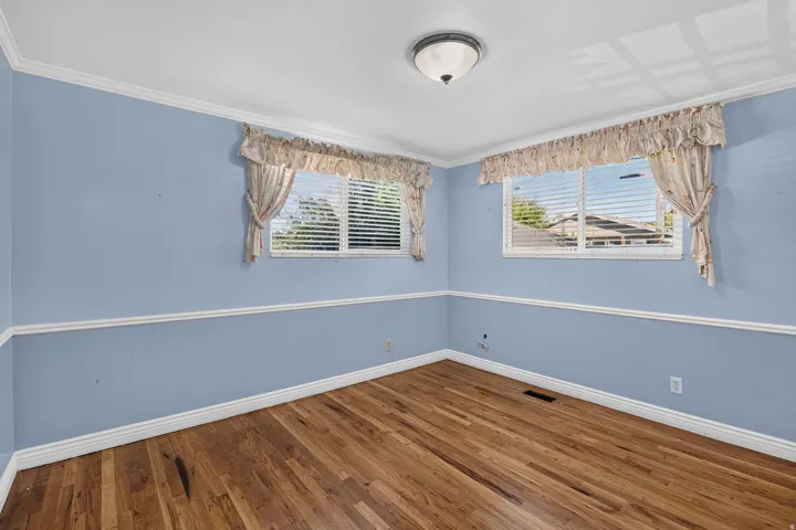 Primary Suite - Hardwood flooring throughout, featuring crown molding, chair rail detailing, and dual windows
