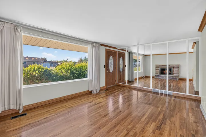 Rich hardwood flooring, large picture window, mirrored wall feature, and main entry door.