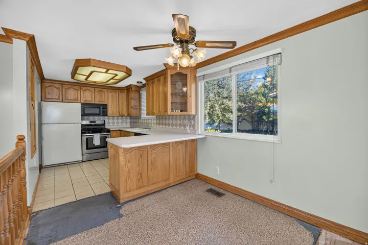 Kitchen featuring wood cabinetry, white countertops, stainless steel appliances, and a ceiling fan with integrated lighting