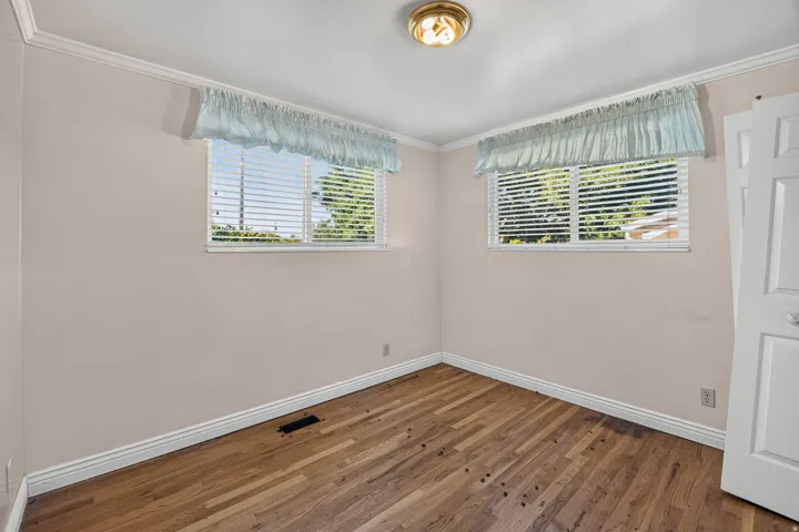 Hardwood flooring, two windows with horizontal blinds, crown molding, and a flush-mount ceiling light fixture