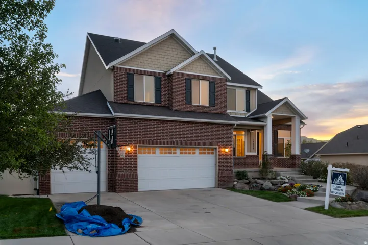 Two-story residence featuring a brick facade, multi-pane windows with dark shutters, a covered entry porch with columns, a multi-car garage, and a concrete driveway