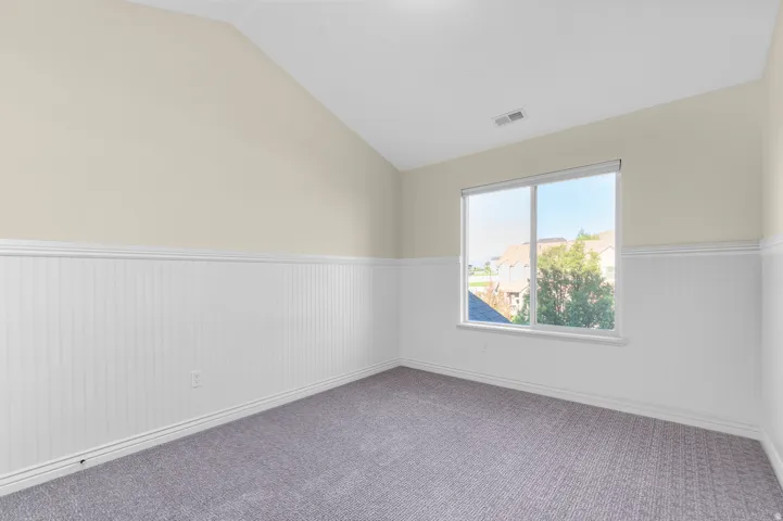 Carpeted room featuring a single window, vaulted ceiling, and wainscoting