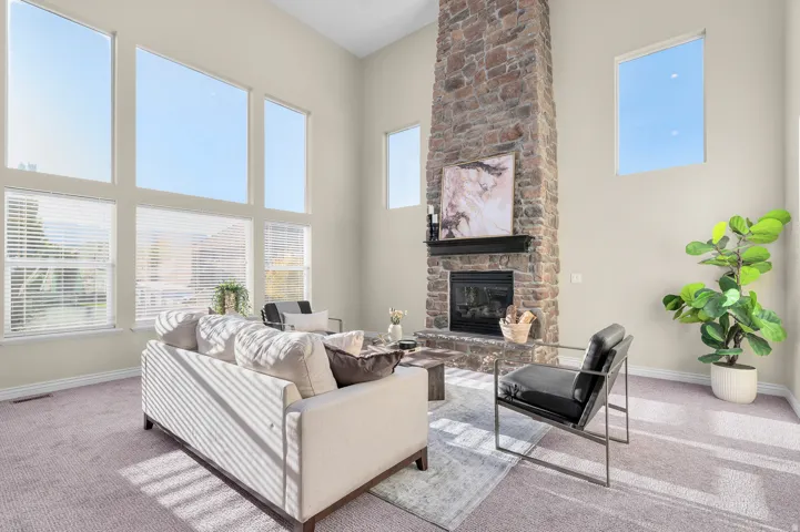 Stone-clad fireplace with dark wood mantel, high vaulted ceilings, and large windows with blinds