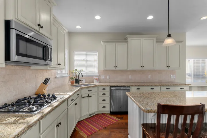 Kitchen featuring light-toned cabinetry, stainless steel appliances, speckled countertops, and a tiled backsplash