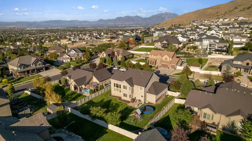 Expansive green lawn with mountain backdrop, fenced yard, and multiple mature trees