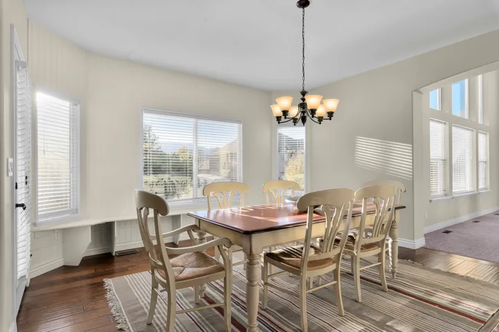 Hardwood flooring, multiple windows with blinds, built-in window bench, chandelier with frosted glass shades, arched doorway
