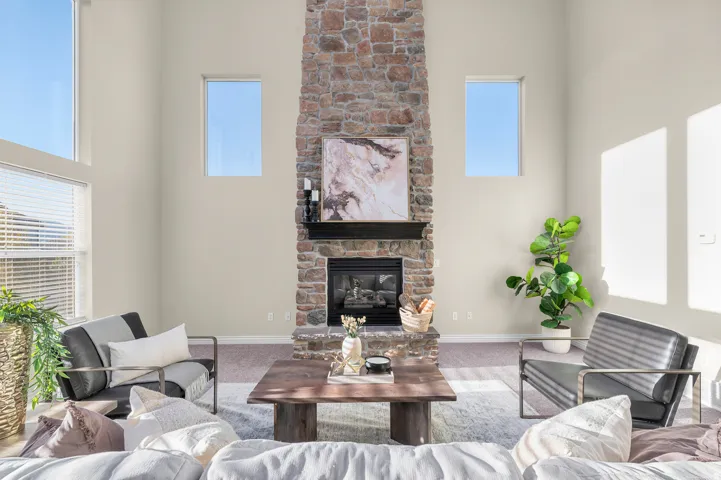 Vaulted ceilings, a full-height stone fireplace, a dark wood mantel, and large windows