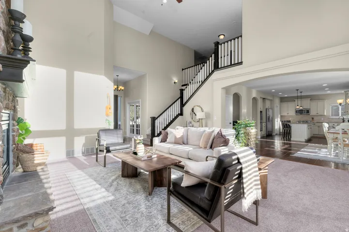 Two-story vaulted ceiling, stone-clad fireplace, hardwood flooring, open concept kitchen, and staircase with white risers and dark wood handrail
