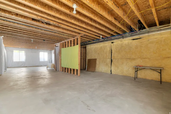 Unfinished basement with exposed wood joists, concrete flooring, and multiple windows