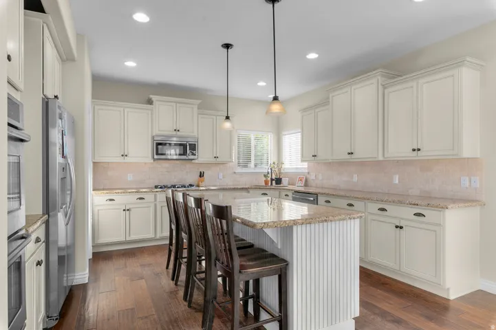 Cream-painted cabinetry, stainless steel appliances, granite countertops, and wood-finish flooring