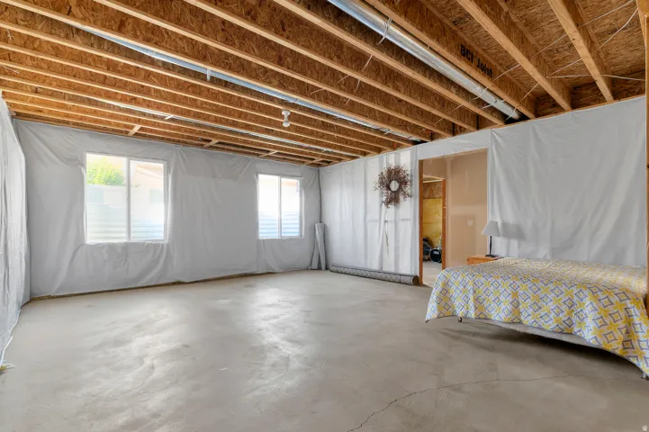 Exposed ceiling joists, two windows with white frames, concrete flooring, and an open doorway