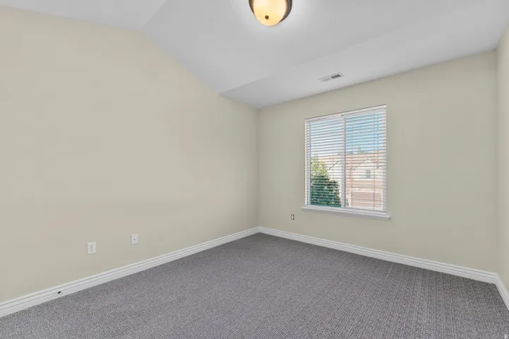 Vaulted ceiling, neutral wall paint, window with blinds, gray carpeting, and a flush mount ceiling light