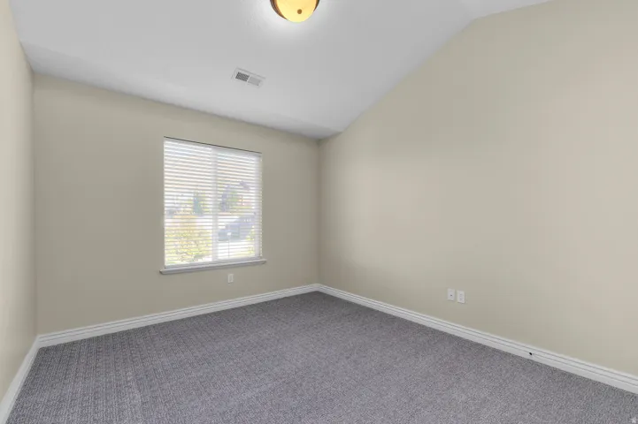 Neutral wall paint, patterned carpeting, sloped ceiling, window with blinds, and flush-mount ceiling light