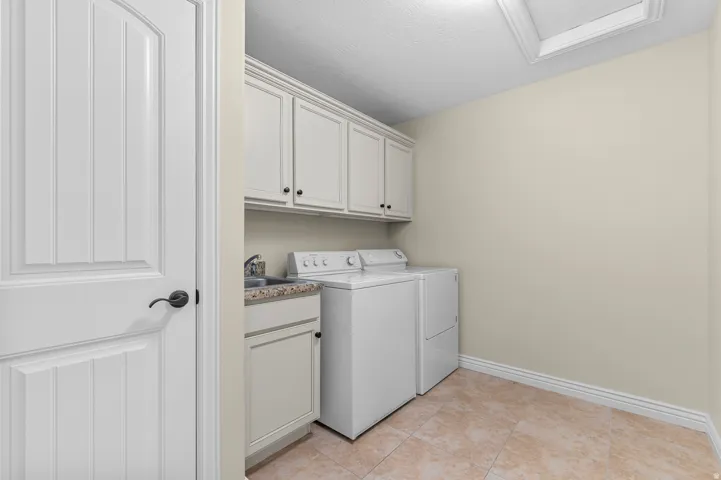 Laundry area featuring white cabinetry with dark hardware, a utility sink with a stone-finish countertop, and tiled flooring