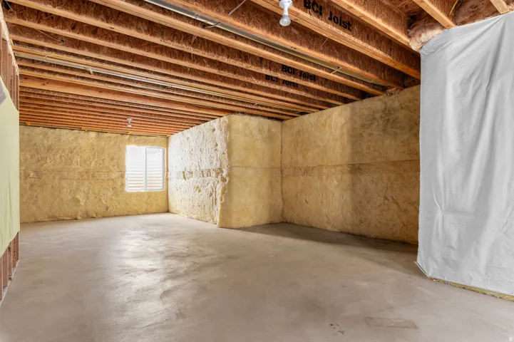 Unfinished lower level featuring exposed wood joists, concrete flooring, and insulated walls