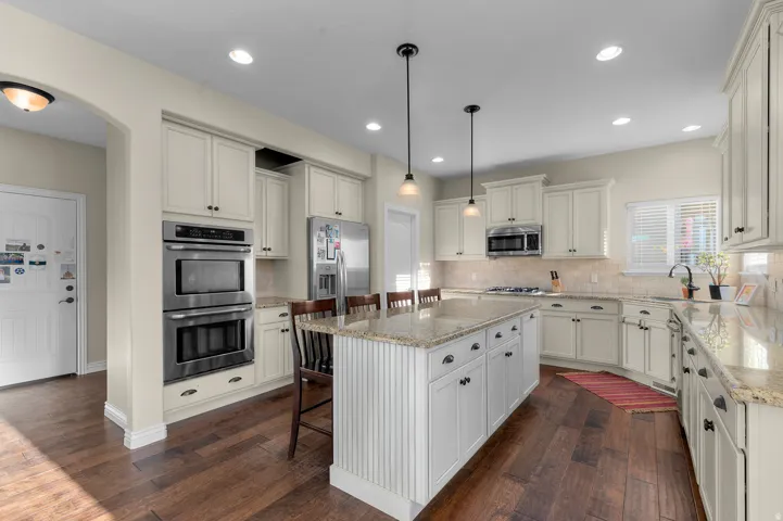 Kitchen featuring wood-finish flooring, an island with pendant lighting, light-toned cabinetry, stainless steel appliances, and light-toned countertops