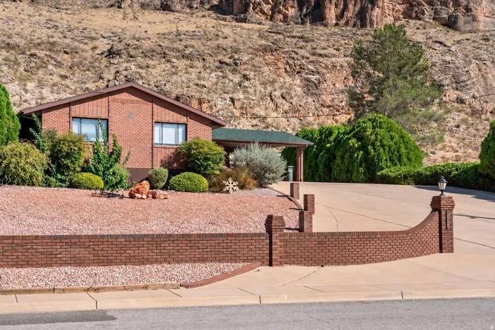 Brick facade property with a covered carport, curved brick retaining wall, and a paved driveway