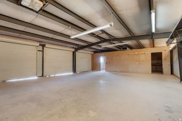 Expansive concrete flooring with multiple roll-up doors, exposed structural beams, fluorescent lighting, and interior partitioned spaces