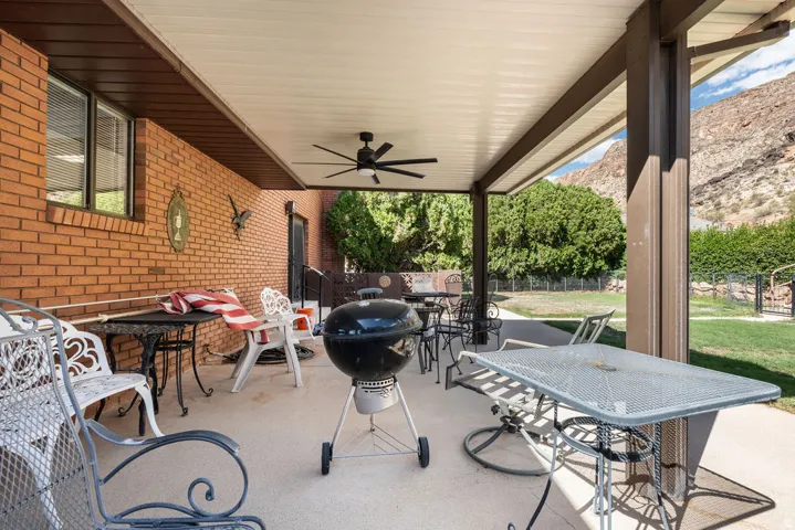 Covered patio with a ceiling fan, brick exterior, concrete flooring, and fenced yard