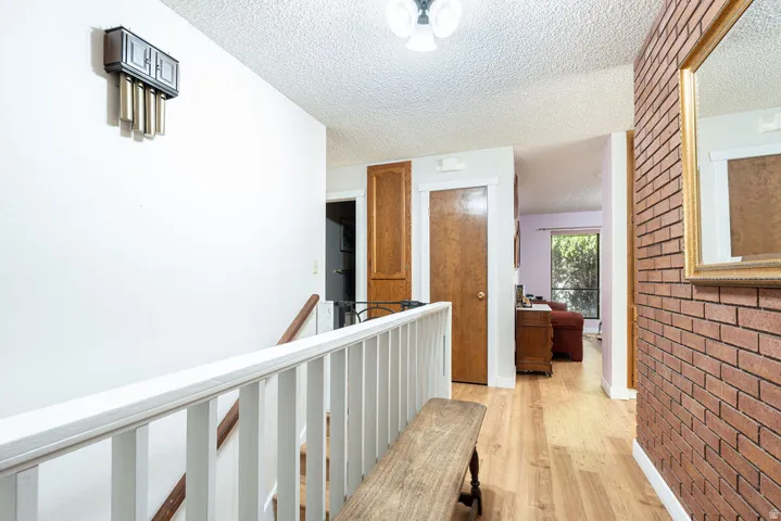 Wood-finish flooring, white painted walls, exposed brick accent wall, and a ceiling-mounted light fixture