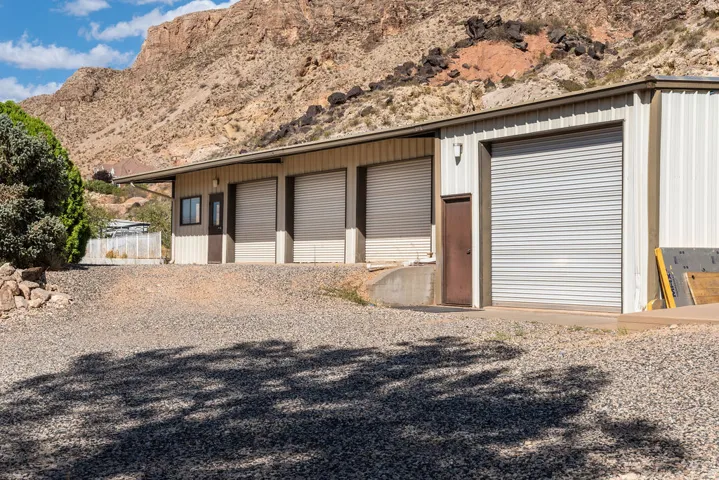 Metal-sided commercial structure featuring multiple roll-up doors, a pedestrian entrance, and a gravel lot